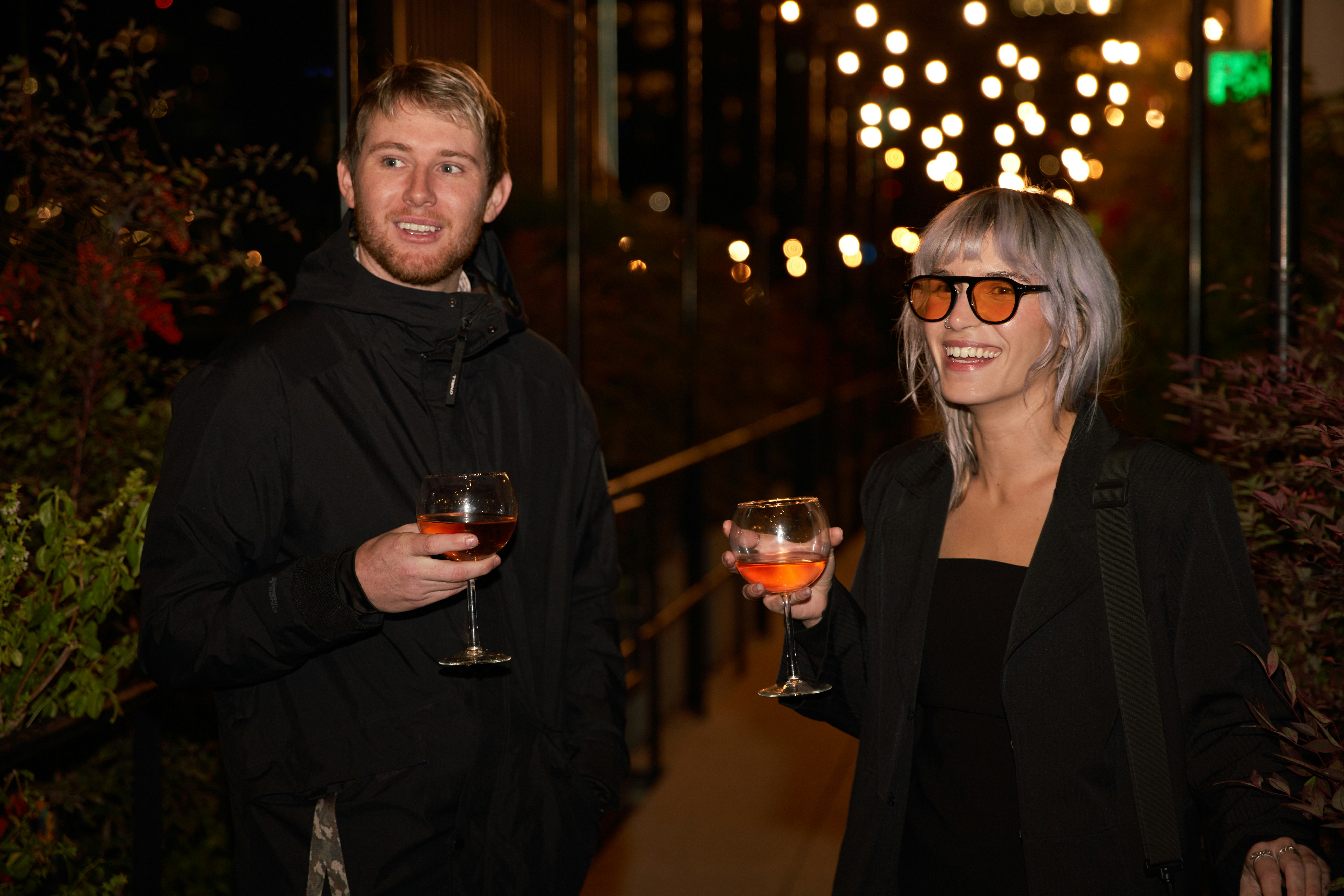 A man and woman laughing outdoors with glasses of rosé wine, highlighting the social preference for real wine and the low and no alcohol alternatives found in the UK.
