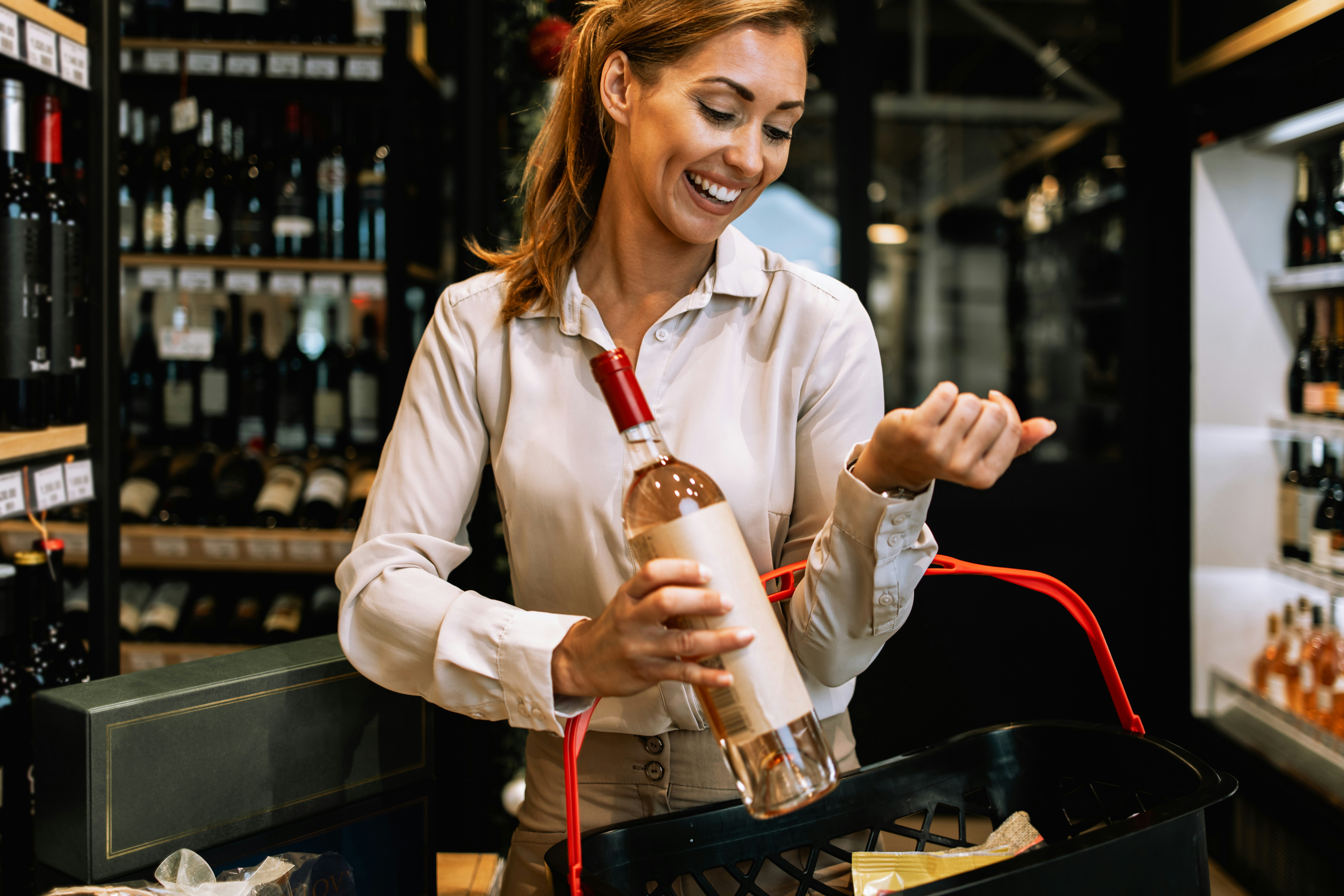 A shopper in a supermarket aisle comparing a bottle's wine price vs wine quality while wondering, "is expensive wine worth it?"