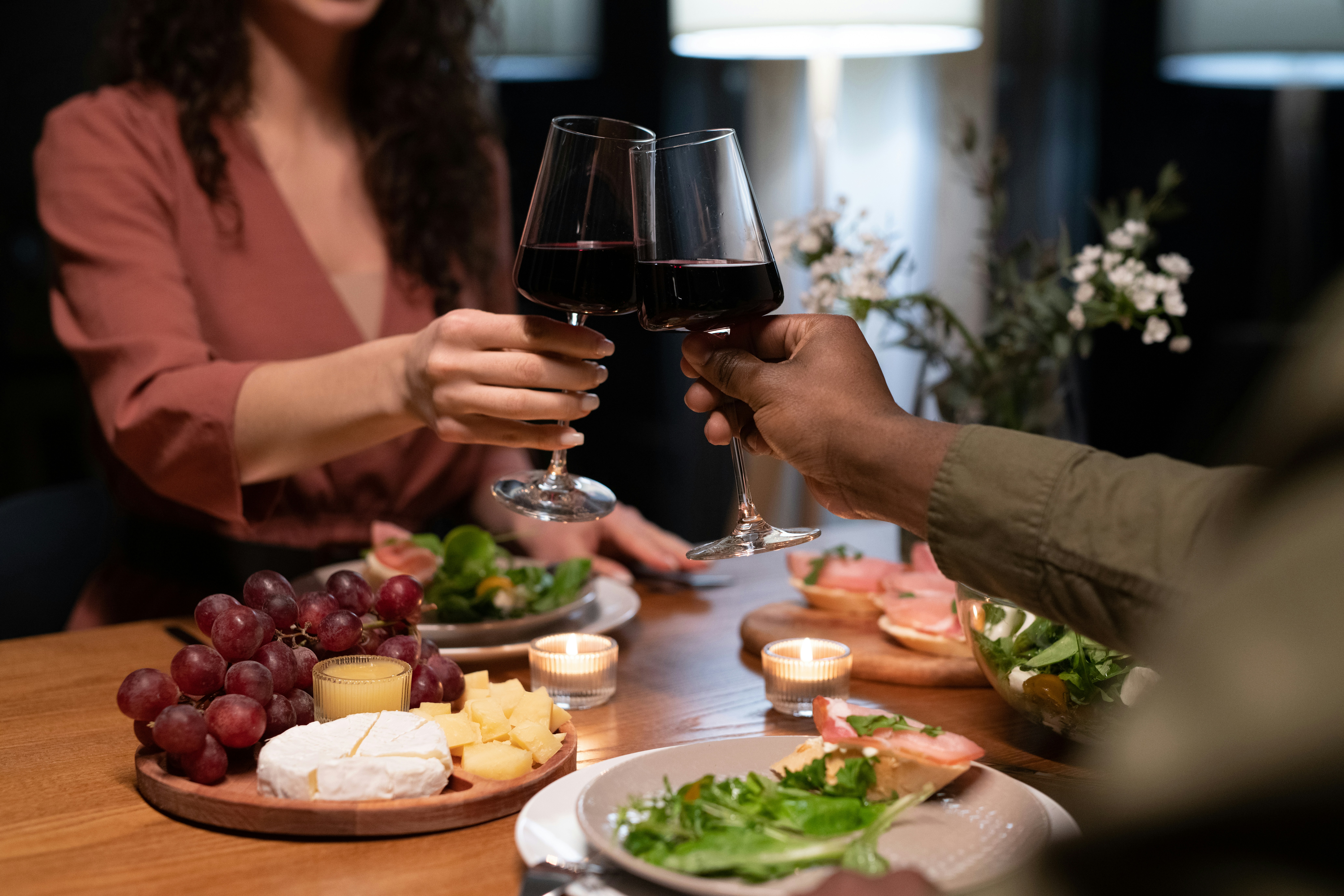 wo people toasting with red wine at a candlelit dinner — eating well is one of the best ways to drink red wine without feeling stuffy